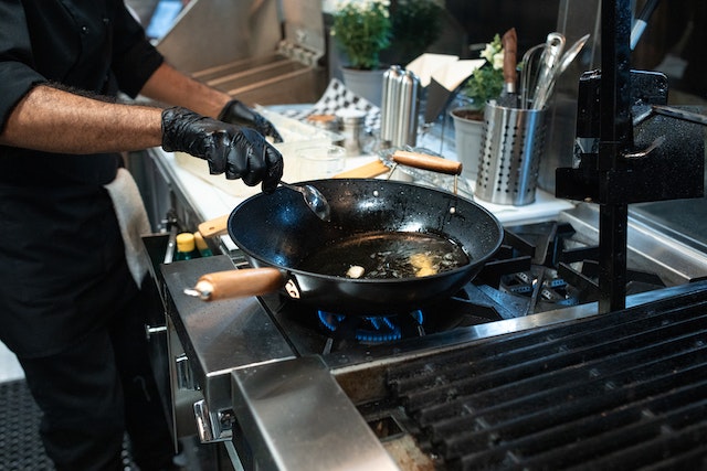 commercial-restaurant-kitchen-cook-holding-frying-pan-over-stove
